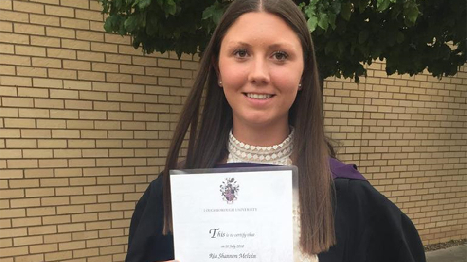 Ria Melvin in her graduation gown, holding her degree certificate.